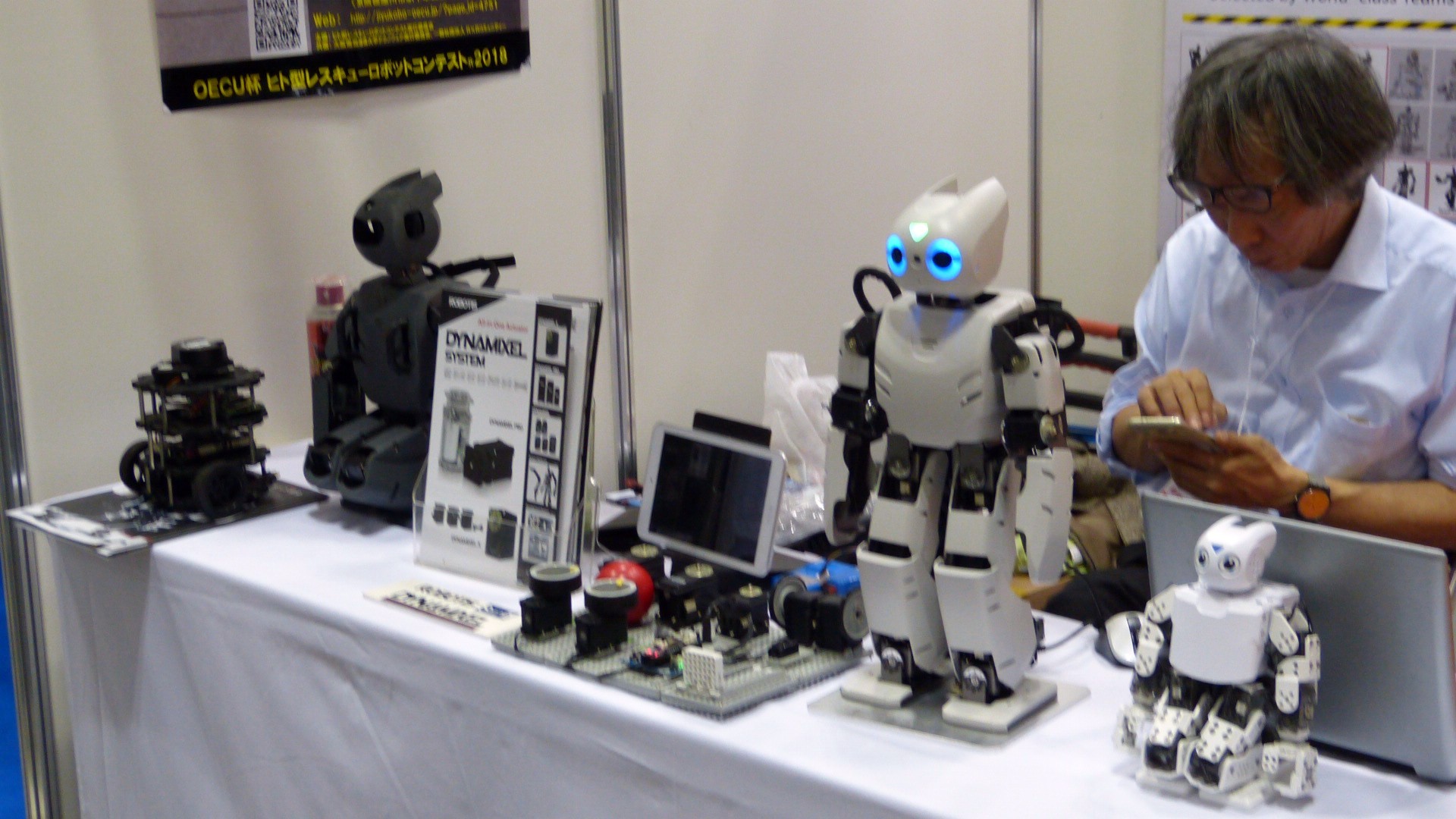 a man uses a smartphone behind a counter of small robots and pamphlets